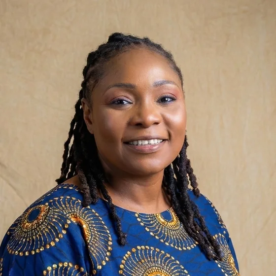 Dr Oluwakemi Damola Adejumo-Ayibiowu, smiling, in an indigo and gold adire-print dress